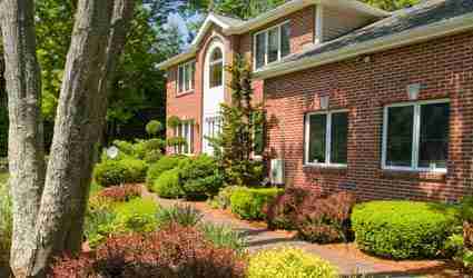 Front yard of brick home with mulch, shrubs and trees