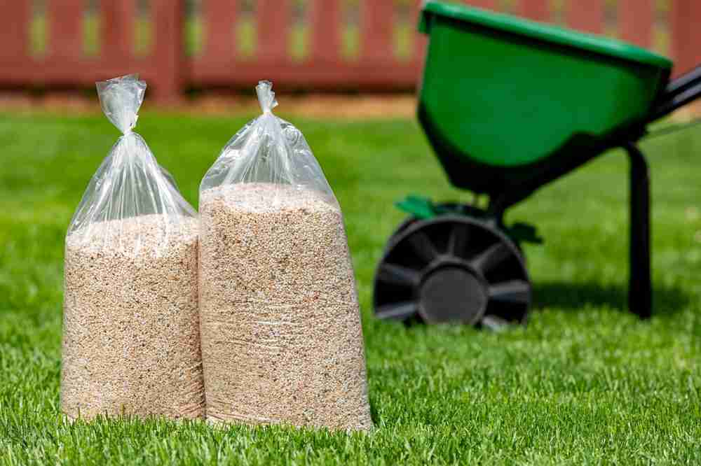 A fertilizer spreader next to two bags of fertilizer and a lawn